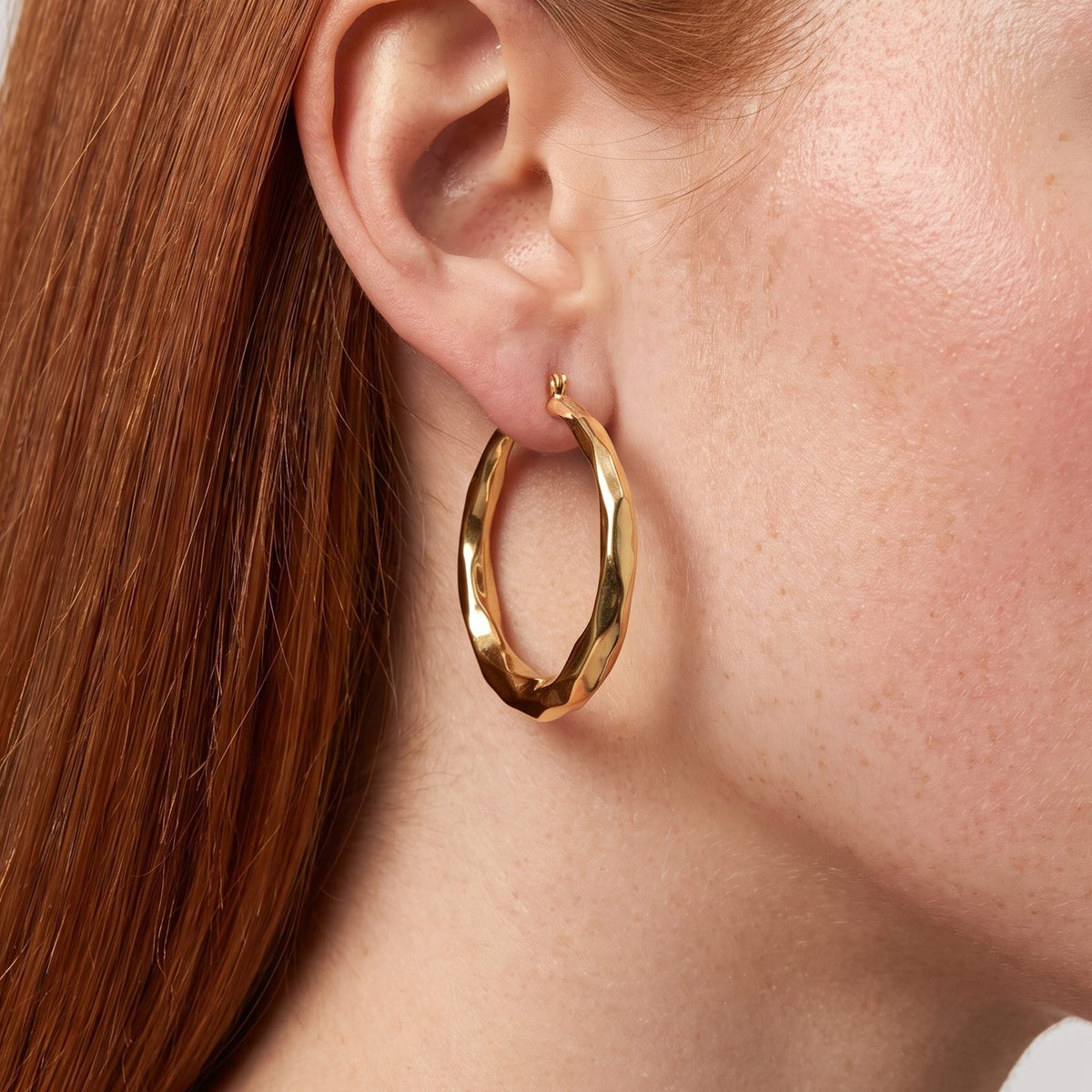 Woman wearing the Aira Hoop Earrings, a twisted gold hoop hanging below the lobe