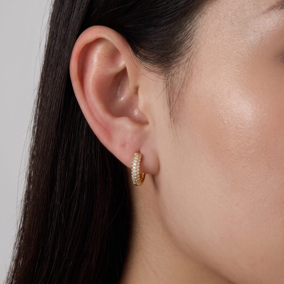 Close view of a woman wearing the Amelia Chunky Crystal Huggies paved with crystals on the lobe