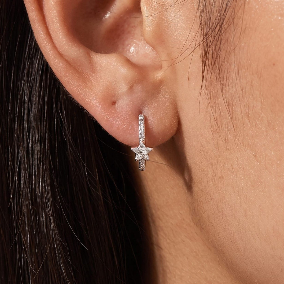 Woman wearing the Anais Crystal Star Hoops on her lobe, featuring a small silver star charm