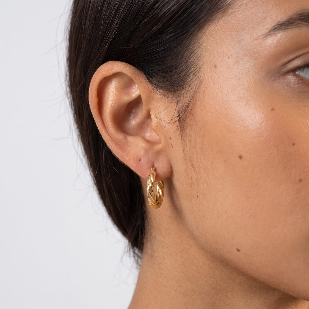Close view of a woman wearing the Camila Twist Gold Hoops with a twisted design through the lobe