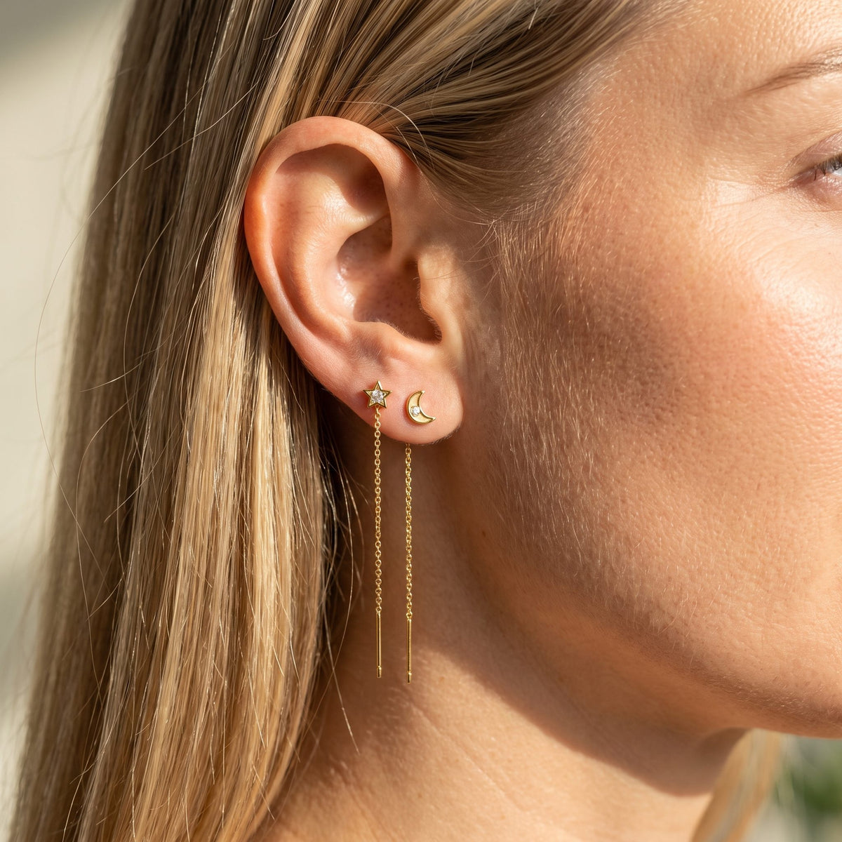 Woman wearing the Camille Drop Chain Earrings hanging below the lobe with star and moon studs