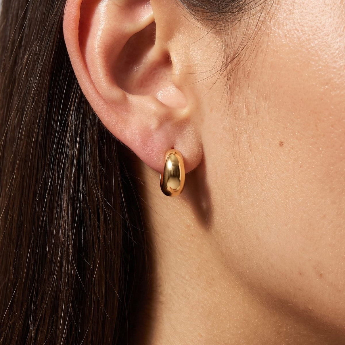 Close view of a woman wearing the Hailey Gold Earrings, a chunky smooth hoop through the lobe