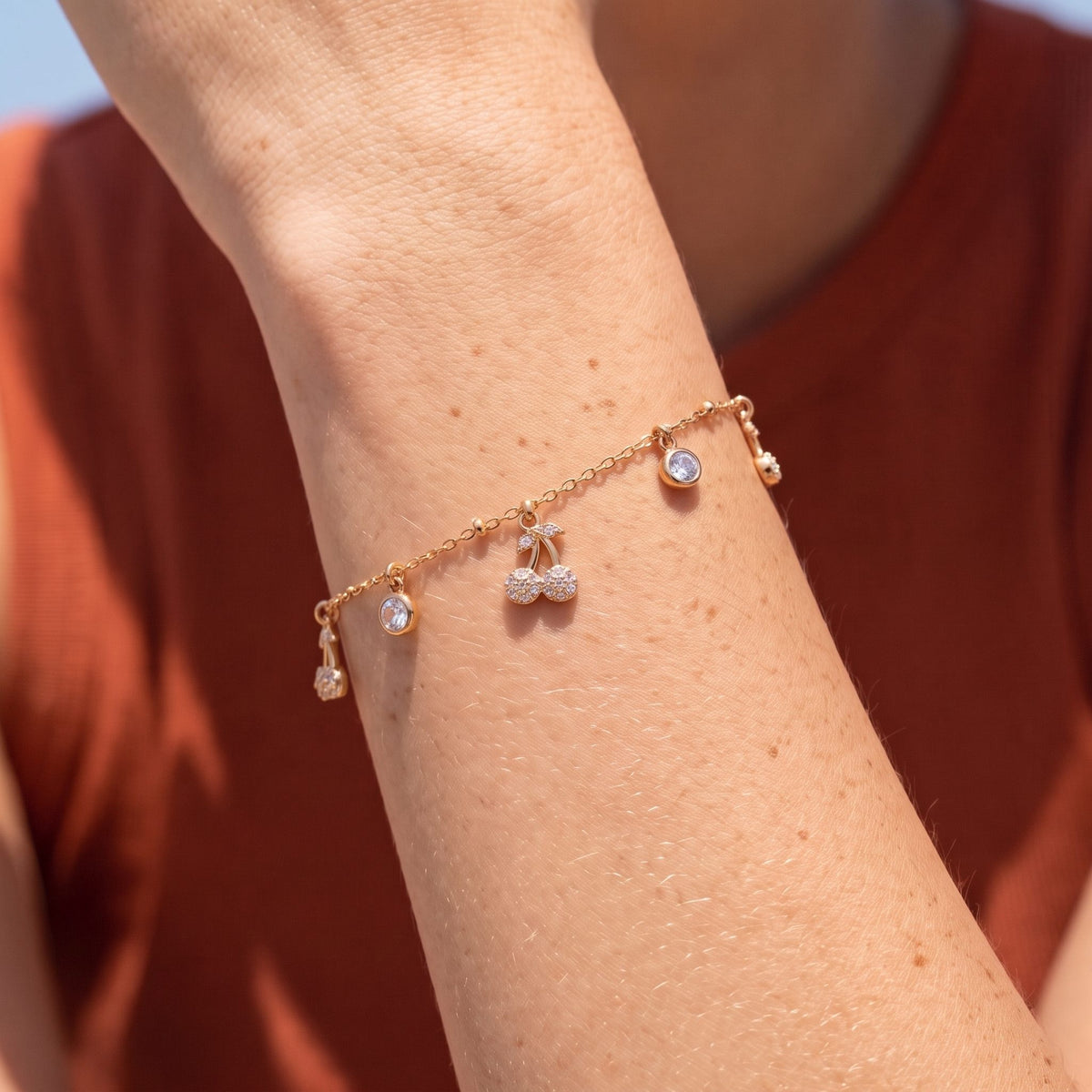 Cherry Charm Bracelet in rose gold worn on the wrist, photographed in natural daylight