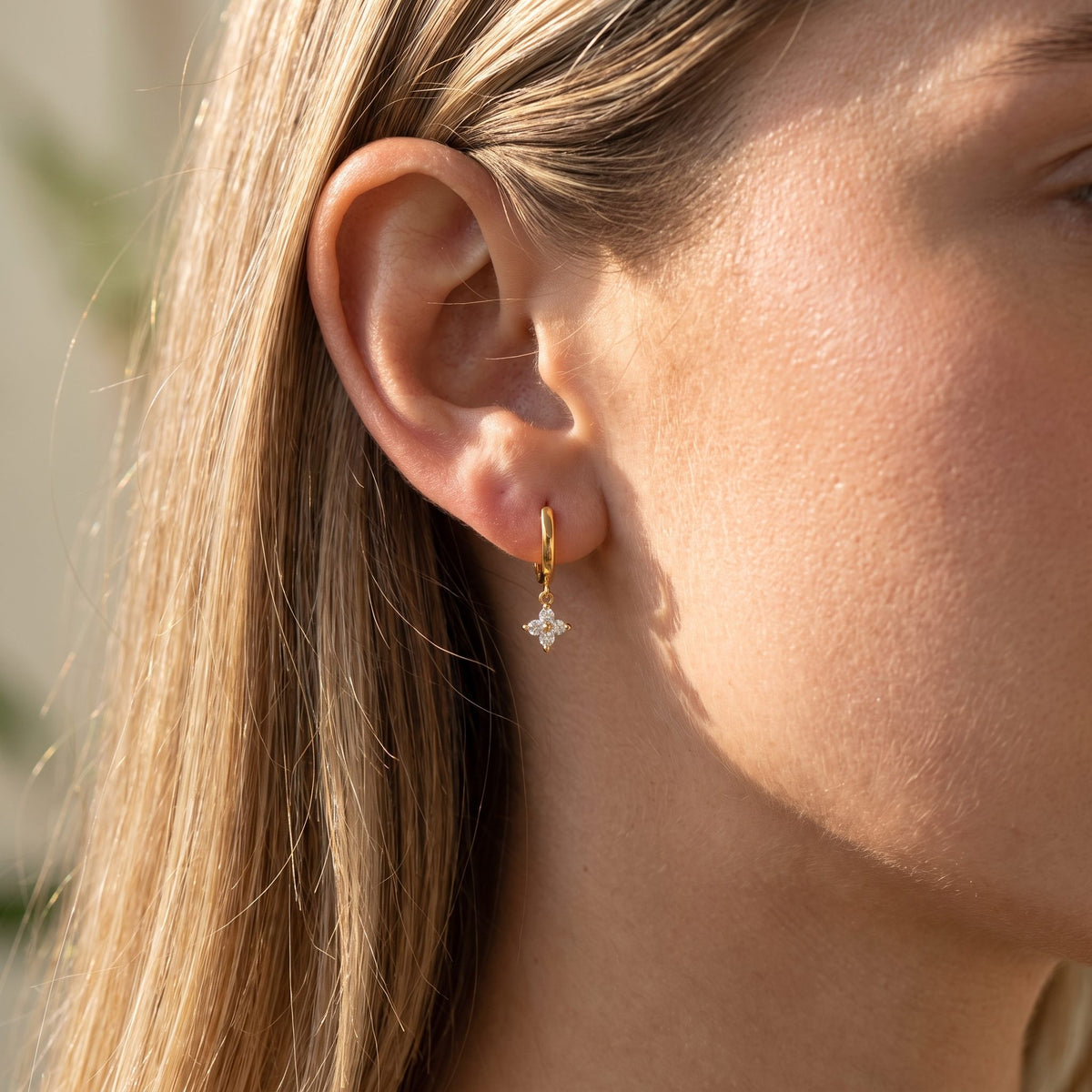 Woman wearing the Chloe Crystal Clover Earrings hanging below the lobe with a gold hoop