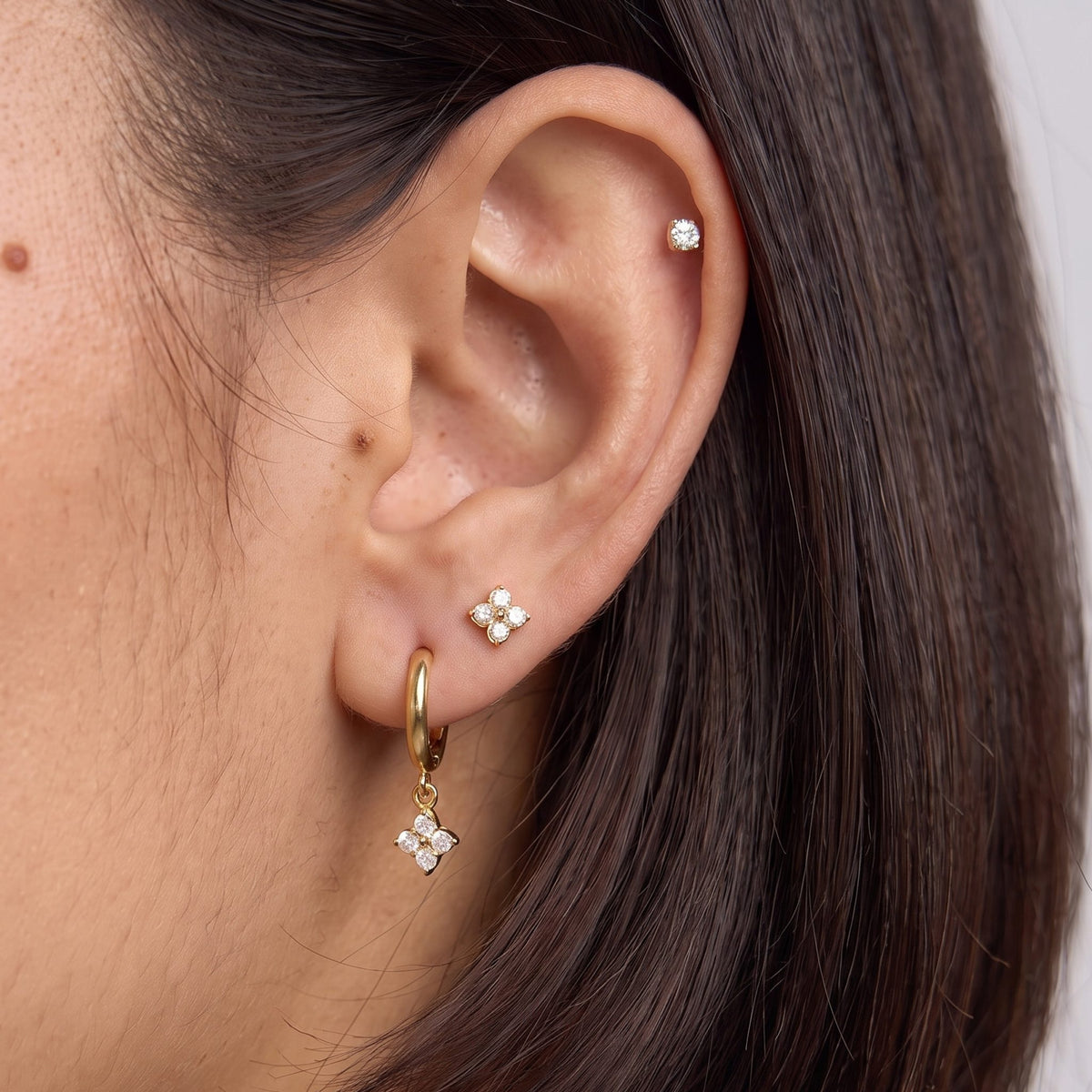 Close-up of the Clover Ear Set on the ear, featuring gold studs and a matching dangling charm with sparkling crystals