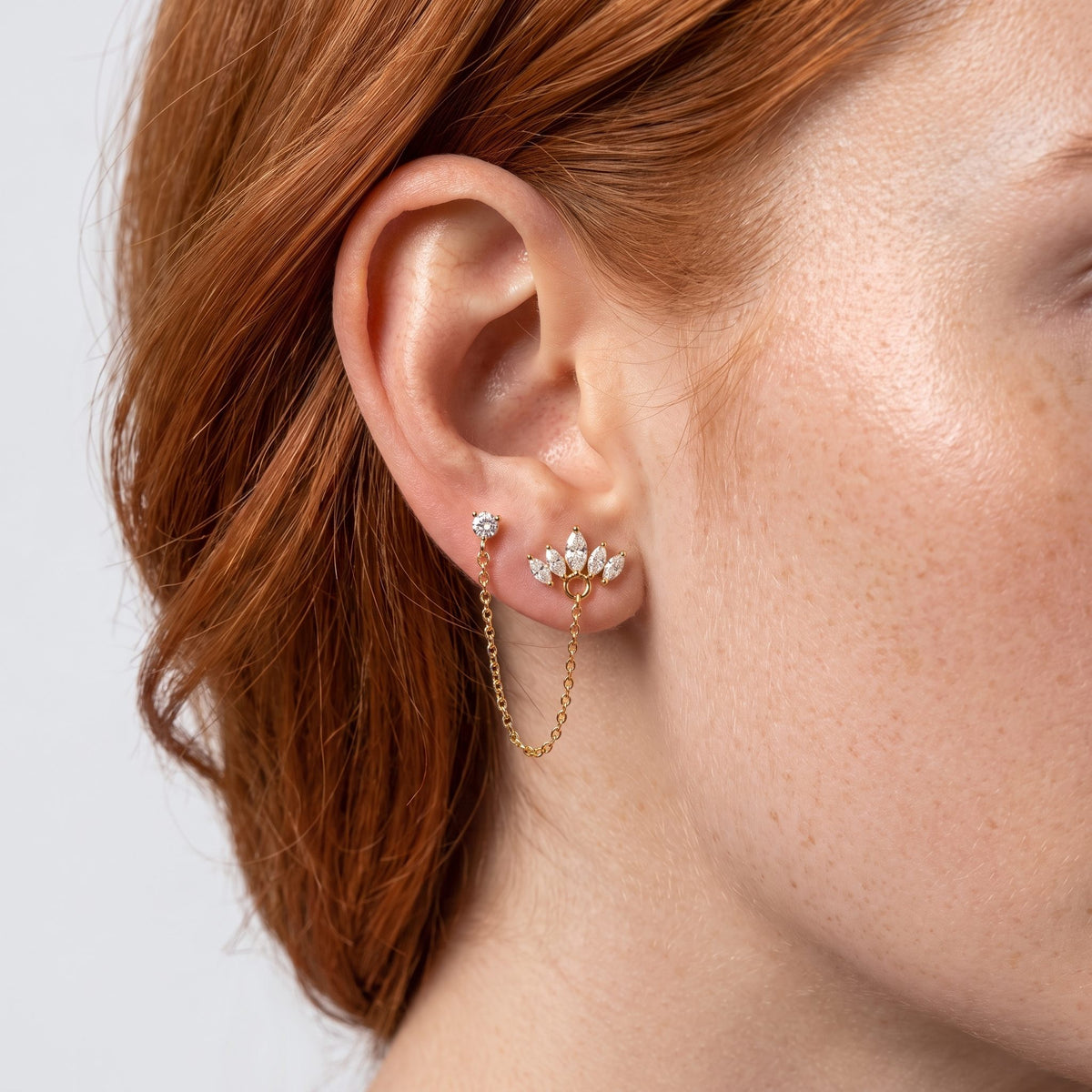 Woman wearing the Colette Crown Crystals Gold Earring on the lobe with a gold chain hanging below