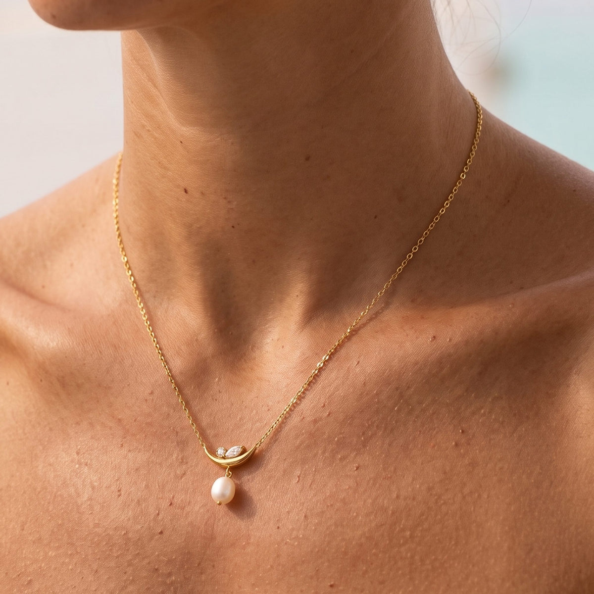 Close-up of the Crescent Pearl Pendant at the collarbone, showing its luminous pearl drop on warm skin