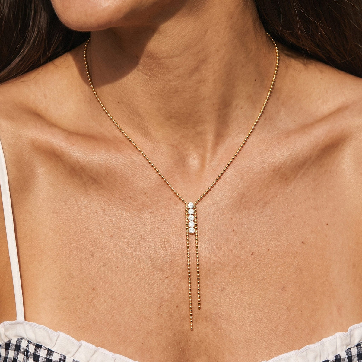 Close-up of the Crystal Bar Lariat Necklace at the collarbone, featuring four sparkling crystals on a gold bead chain