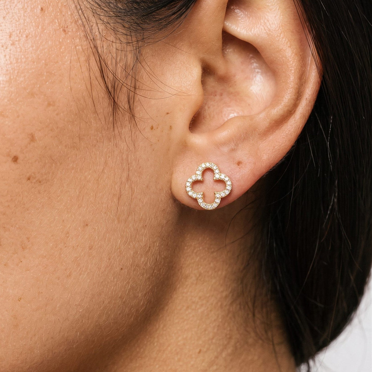 Woman wearing the Daniella Crystal Clover Earrings flat to the lobe with a gold openwork design