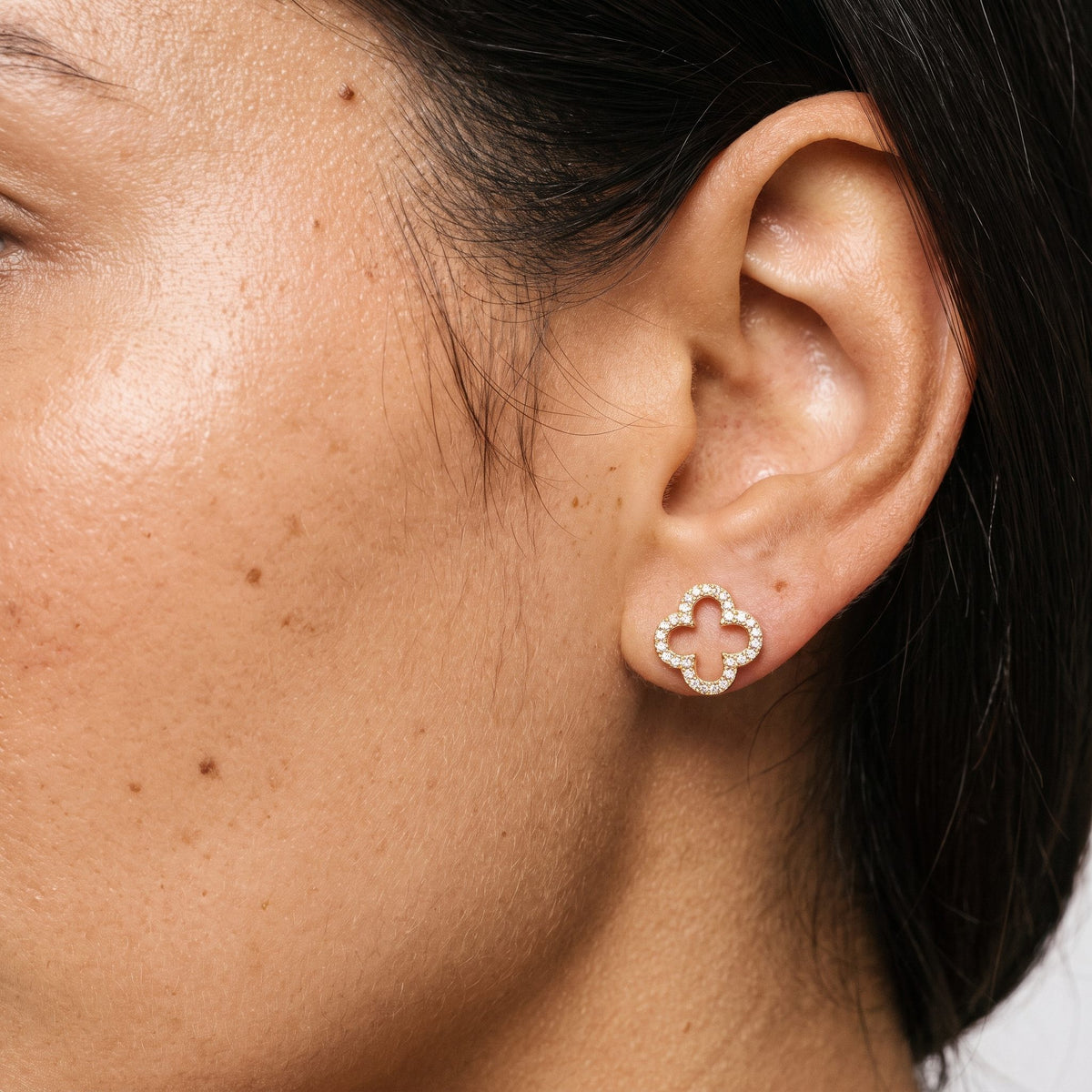 Woman wearing the Daniella Crystal Clover Earrings flat to the lobe with a gold openwork design