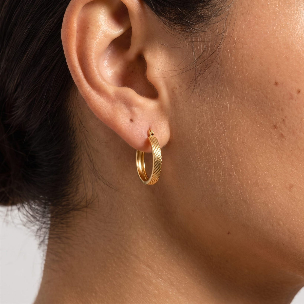 Woman wearing the Elanor Gold Hoop Earrings through the lobe, featuring a textured ribbed pattern
