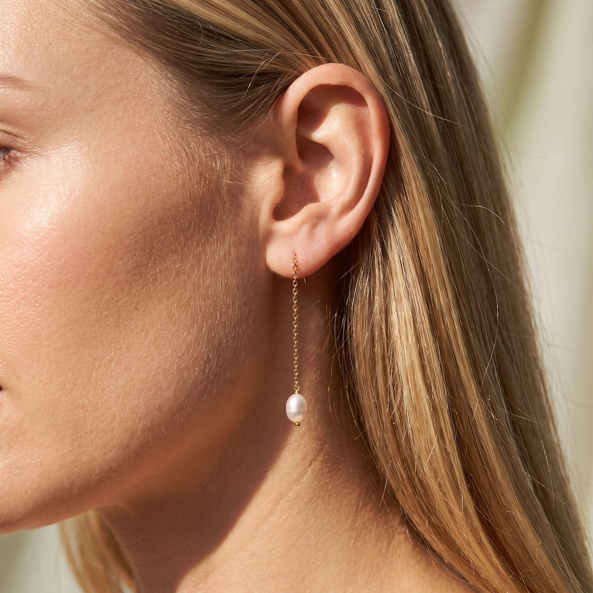 Woman wearing the Élise Dainty Pearl Earrings hanging below the lobe on a delicate gold chain