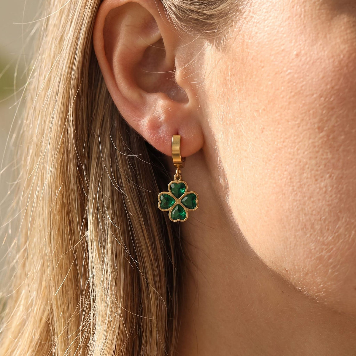Woman wearing the Ella Emerald Clover Earrings hanging below the lobe on a gold hoop