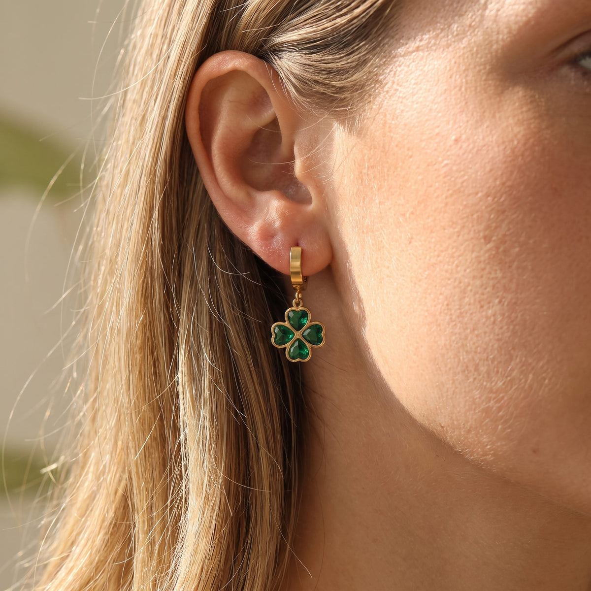 Woman wearing the Ella Emerald Clover Earrings hanging below the lobe on a gold hoop