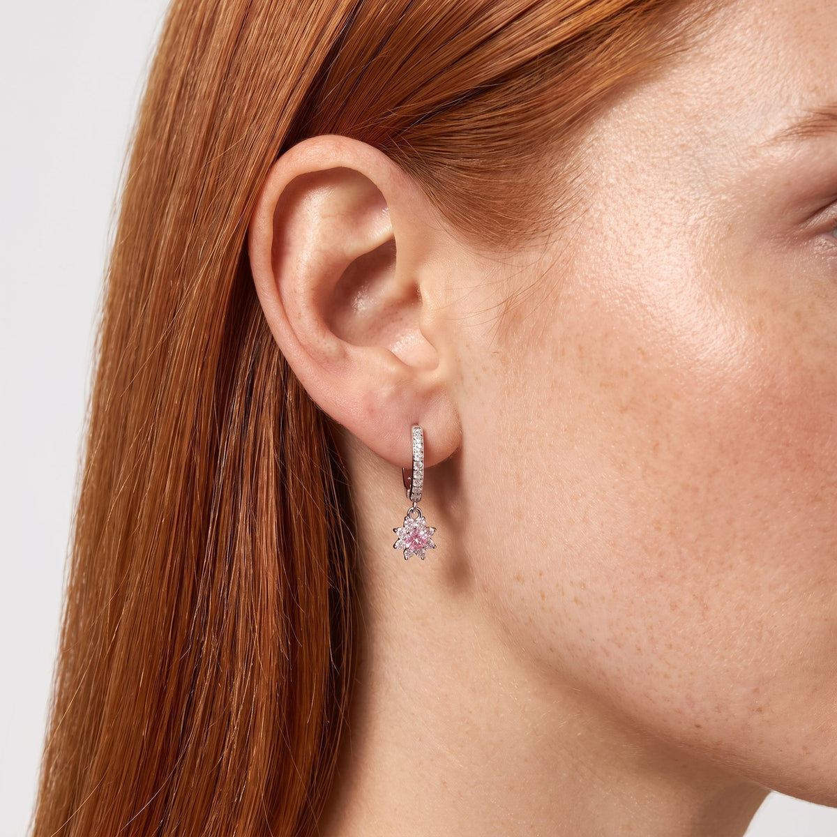 Woman wearing the Élodie Rosé Crystal Hoops hanging below the lobe with a pink flower charm