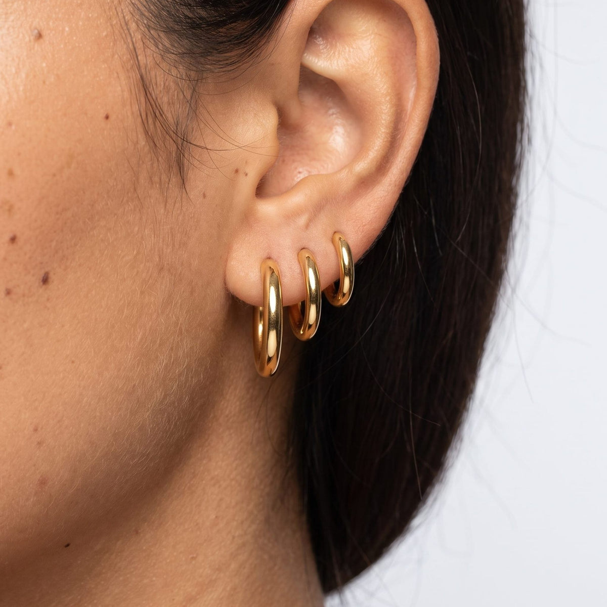 Close view of a woman wearing the Emilie Classic Round Hoops in gold through the lobe