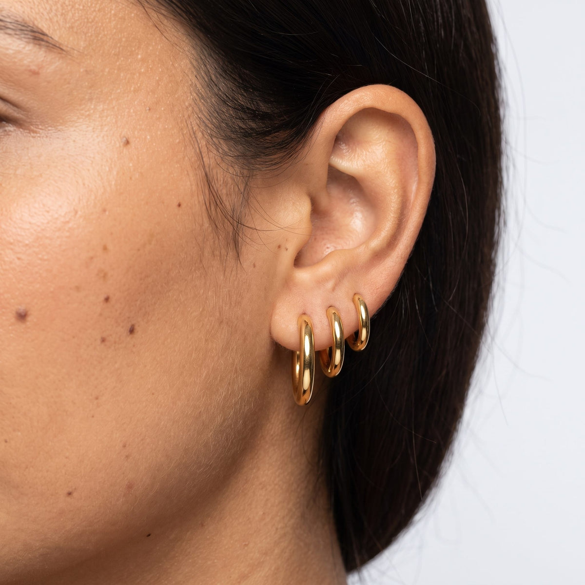 Close view of a woman wearing the Emilie Classic Round Hoops in gold through the lobe
