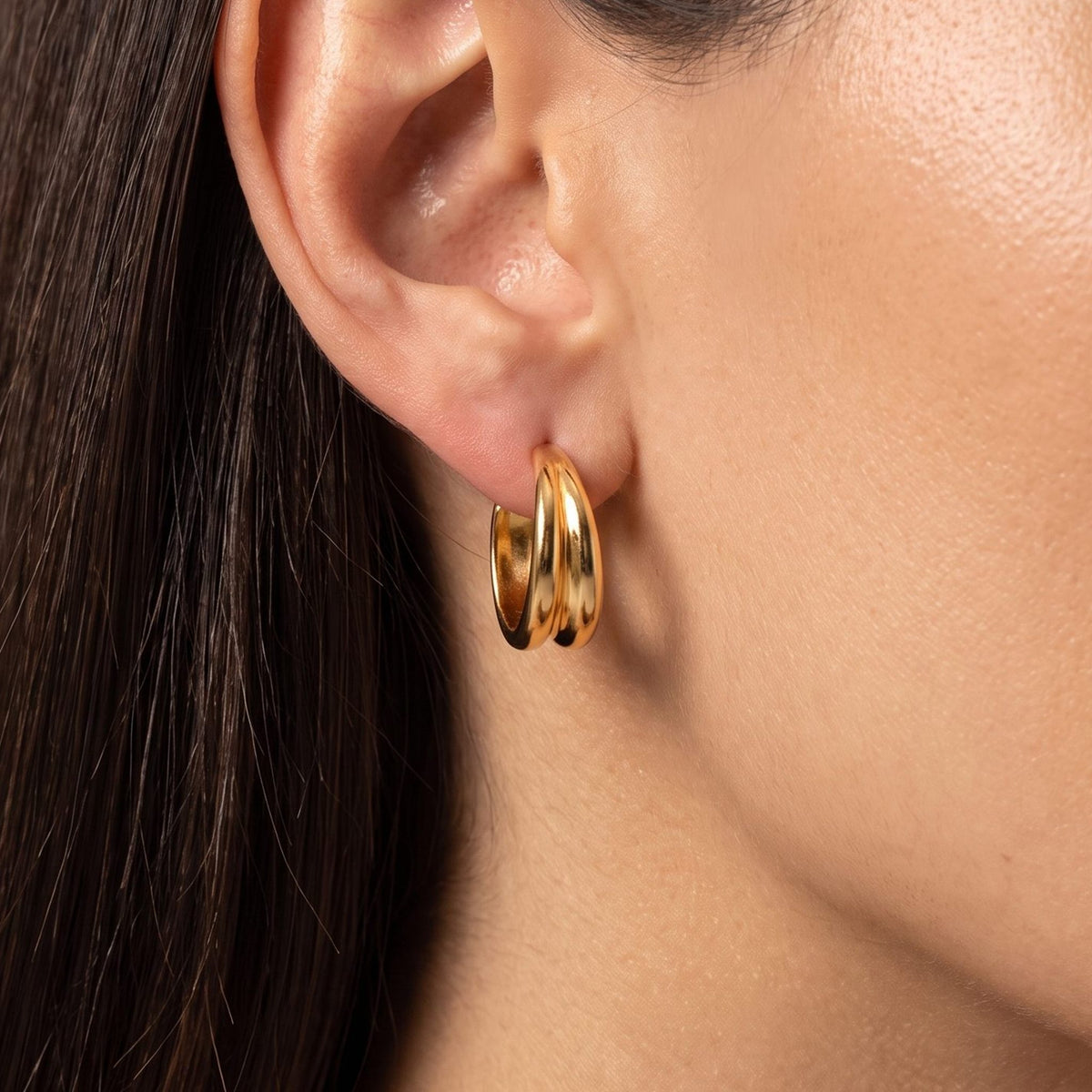 Close view of a woman wearing the Emily Wave Earrings, a gold double hoop through the lobe