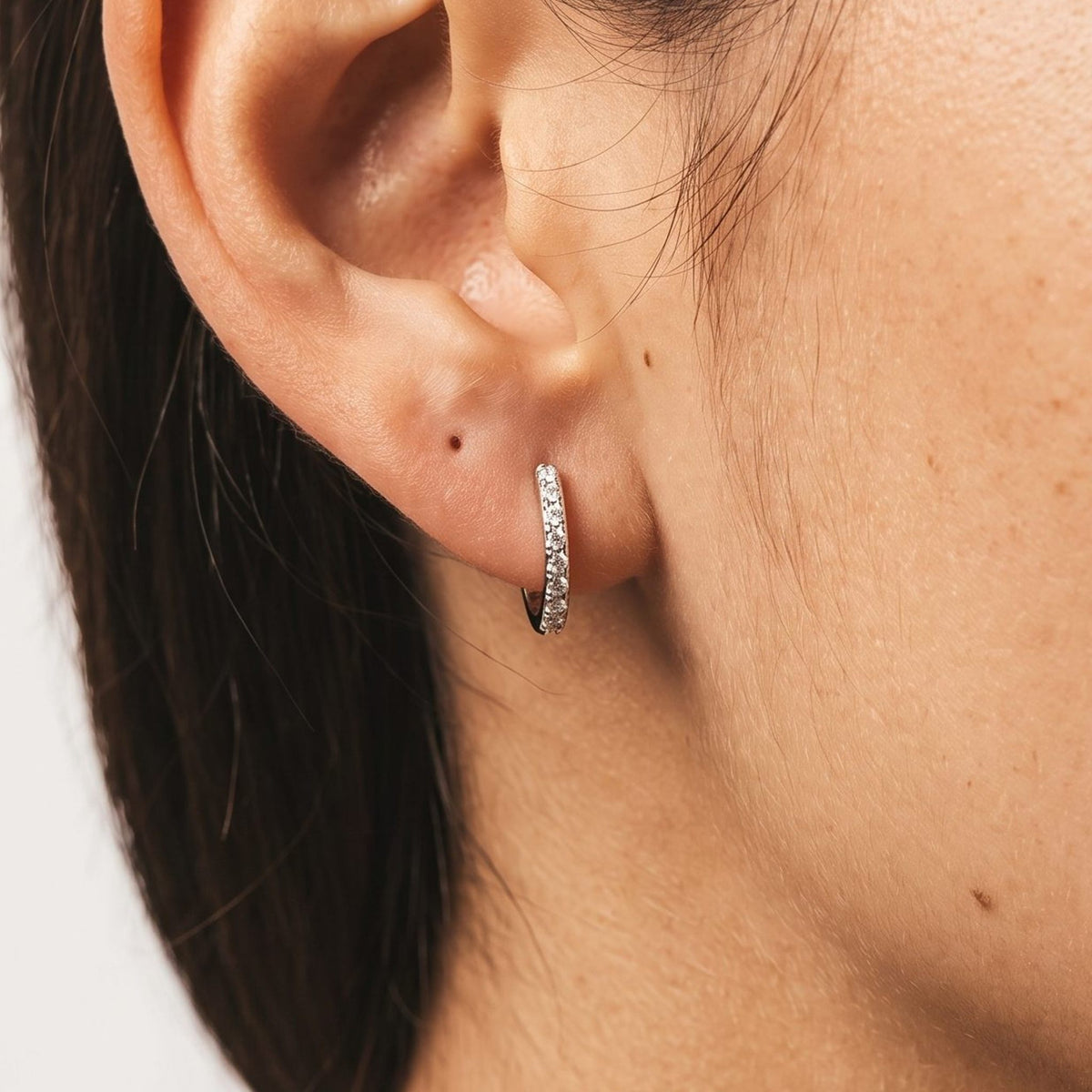 Close view of a woman wearing the Emma Pavé Silver Hoops through the lobe with tiny shimmering stones