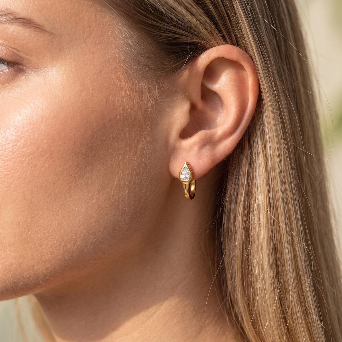 Woman wearing the Geometric Pear Huggies on her ear with straight blonde hair tucked behind it