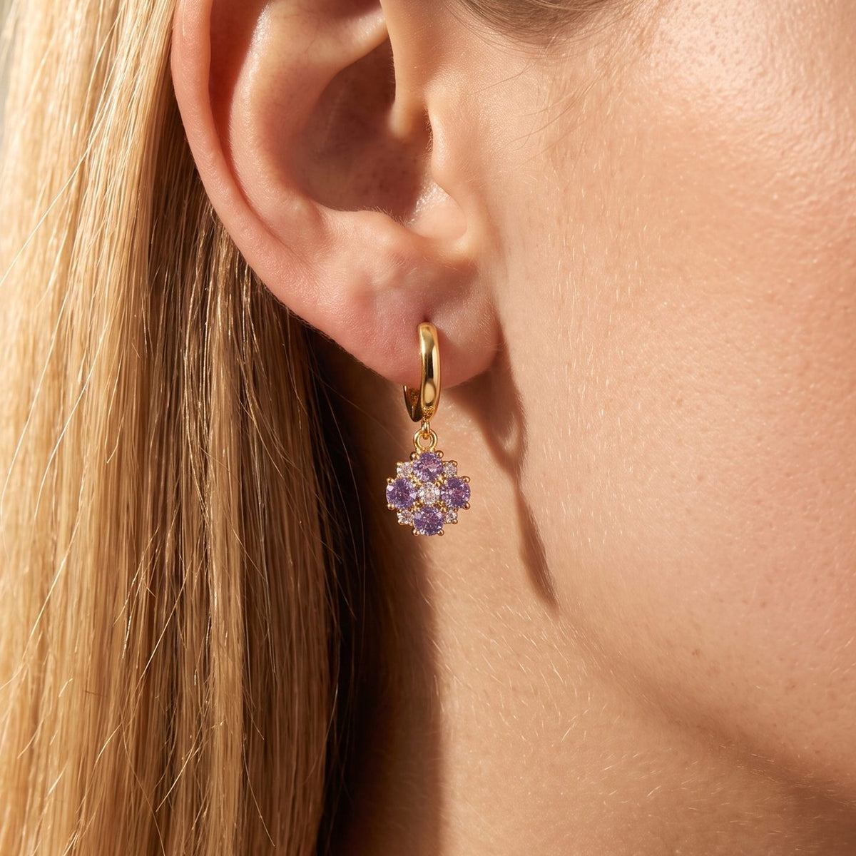 Woman wearing the Giulia Lavender Crystal Earrings, featuring a purple flower charm hanging below the lobe