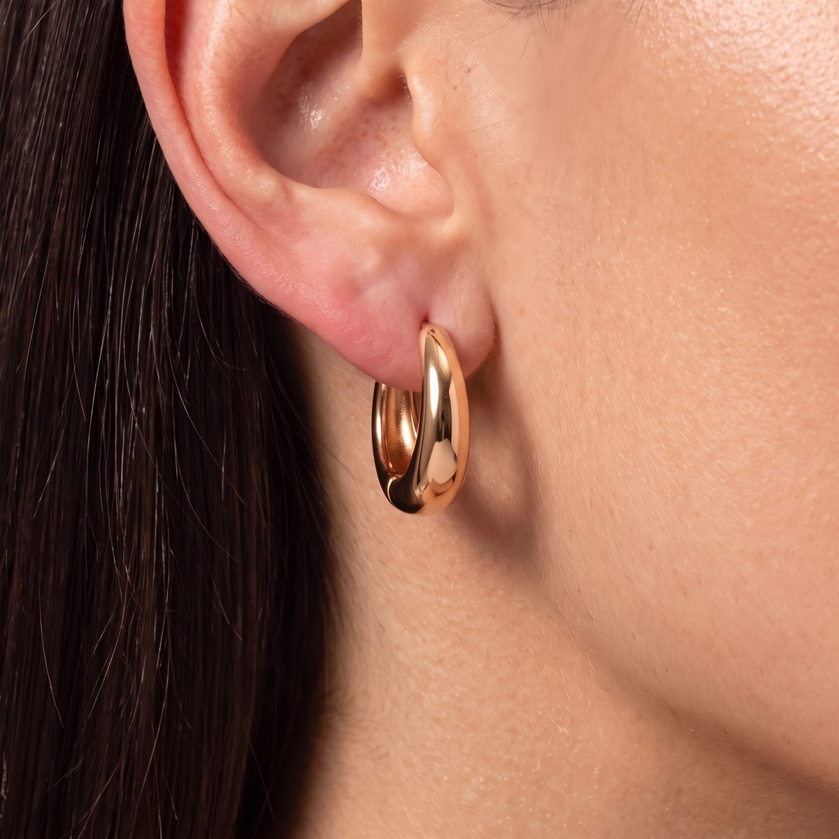 Close-up of the rose gold Dome Hoops on an ear, showing their smooth, polished shine
