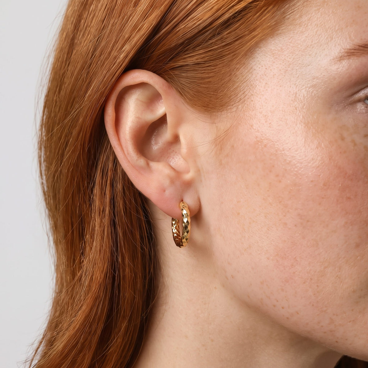 Woman wearing the Hanna Hoops Earrings, a textured gold hoop hanging below the lobe
