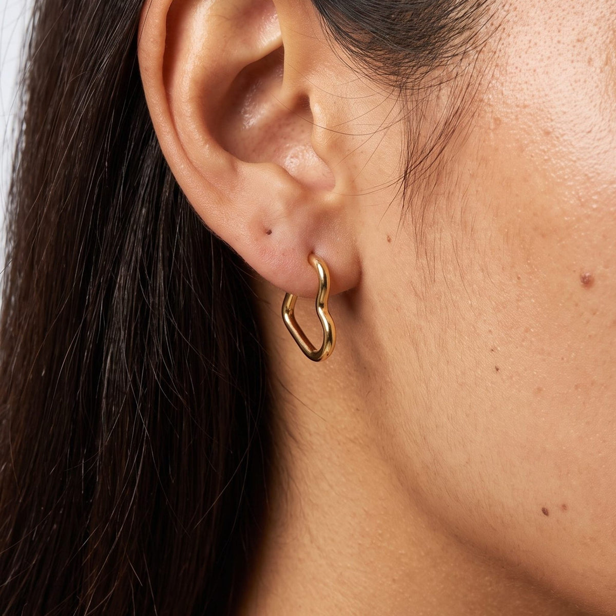 Woman wearing the Helena Heart Hoops, a gold heart-shaped earring hanging below the lobe