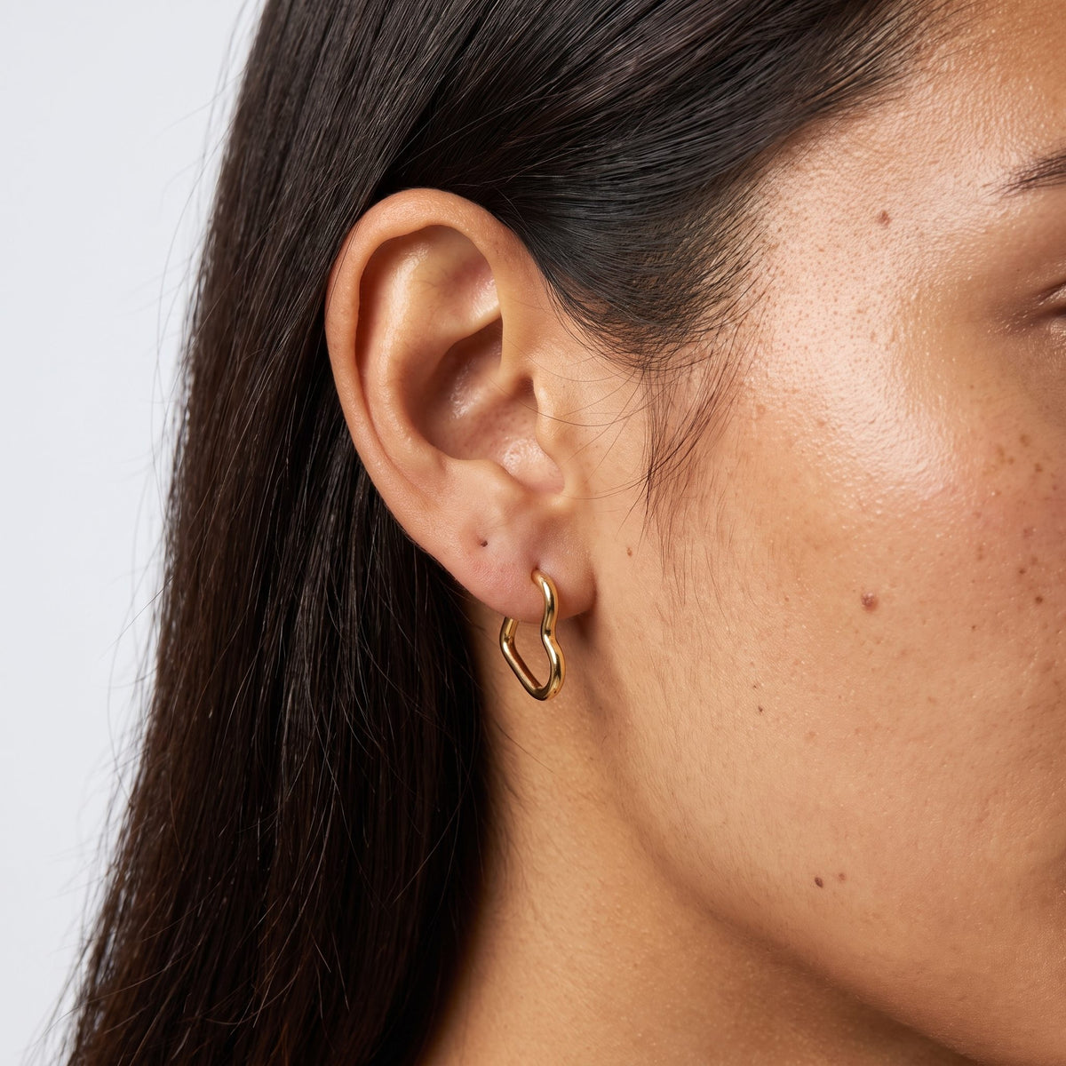 Woman wearing the Helena Heart Hoops, a gold heart-shaped earring hanging below the lobe