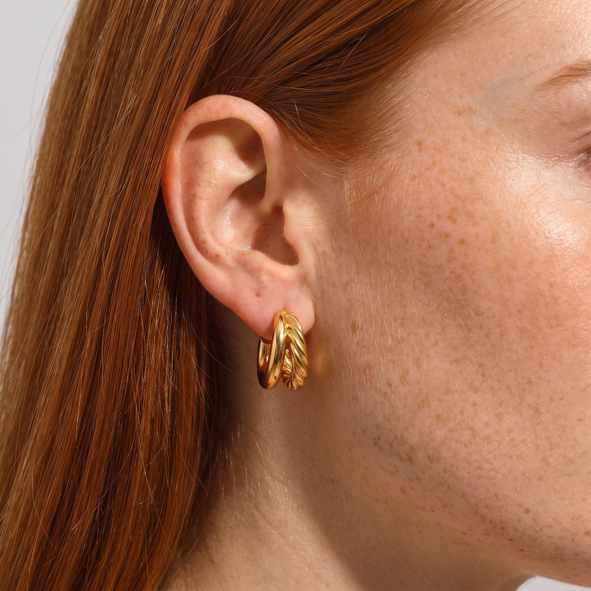 Woman wearing the Juliet Layered Gold Earrings on her lobe, featuring a smooth and a twisted hoop