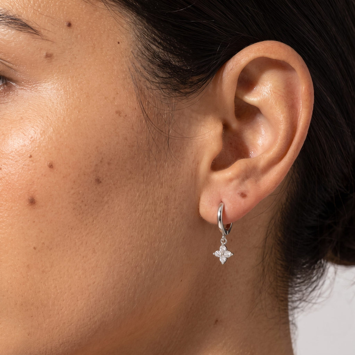 Woman wearing the Juliette Clover Crystal Hoops through the lobe with a silver clover charm hanging below
