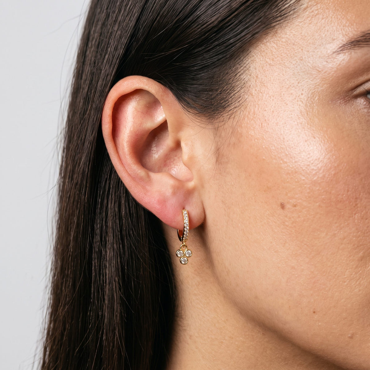 Woman wearing the Juliette Triple Stone Earrings hanging below the lobe with a gold three-stone charm