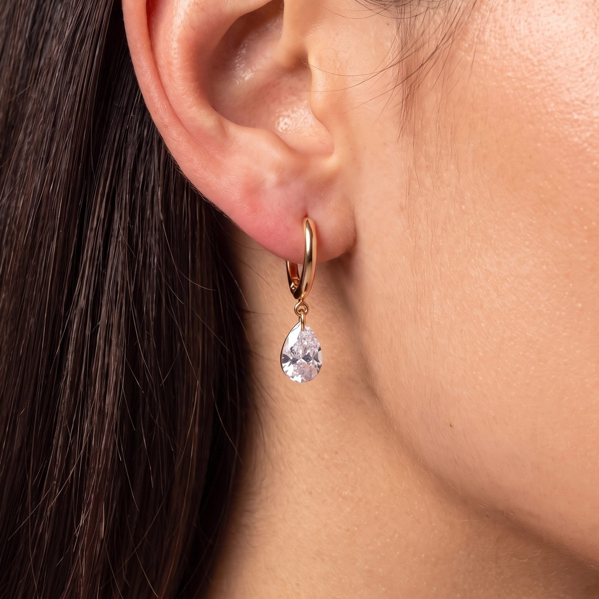 Close-up of the Large Teardrop Huggies on the ear showing a dangling crystal teardrop charm, in rose gold