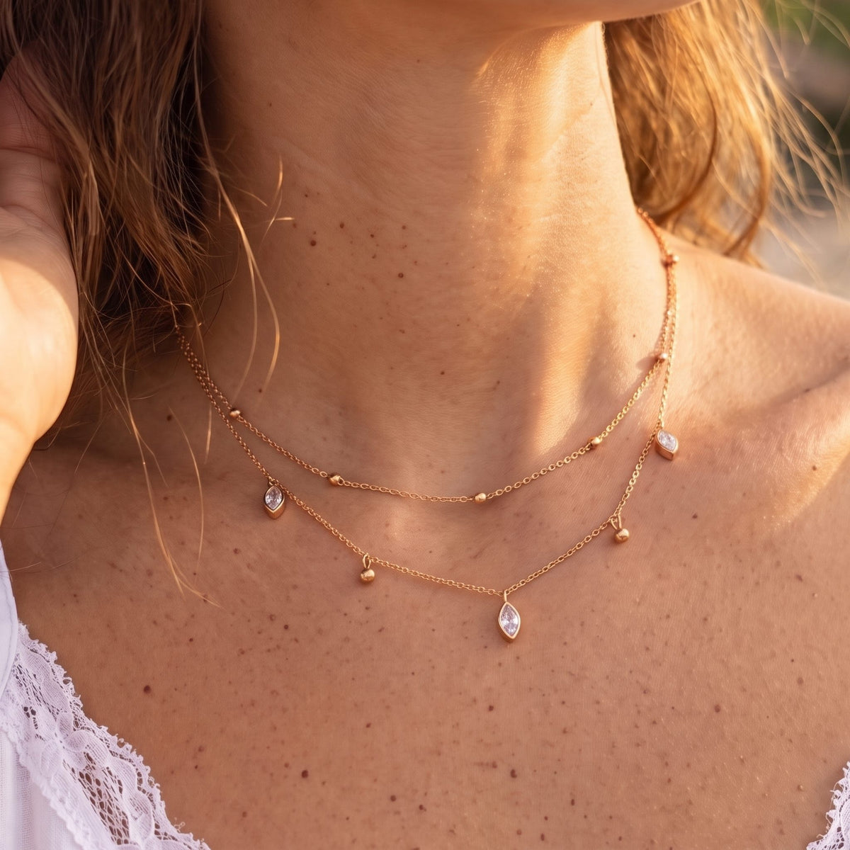 Close-up of the Layered Marquise Necklace worn at the collarbone, highlighting its dangling crystals in golden light, in rose gold