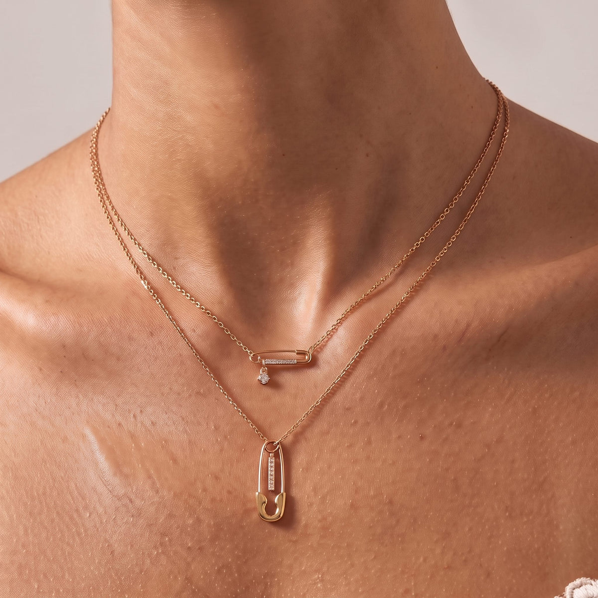 Close-up of the Layered Safety Pin Necklace at the collarbone showing the crystal-embellished charms, in rose gold