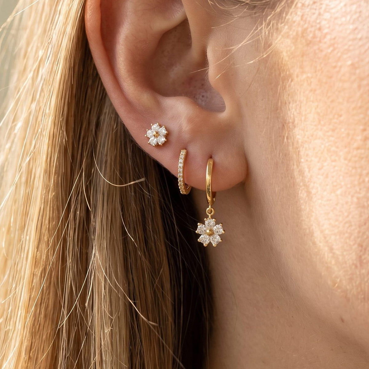 Close view of a woman wearing the Lilly Crystal Flower Earrings Set with gold flower charms on the lobe