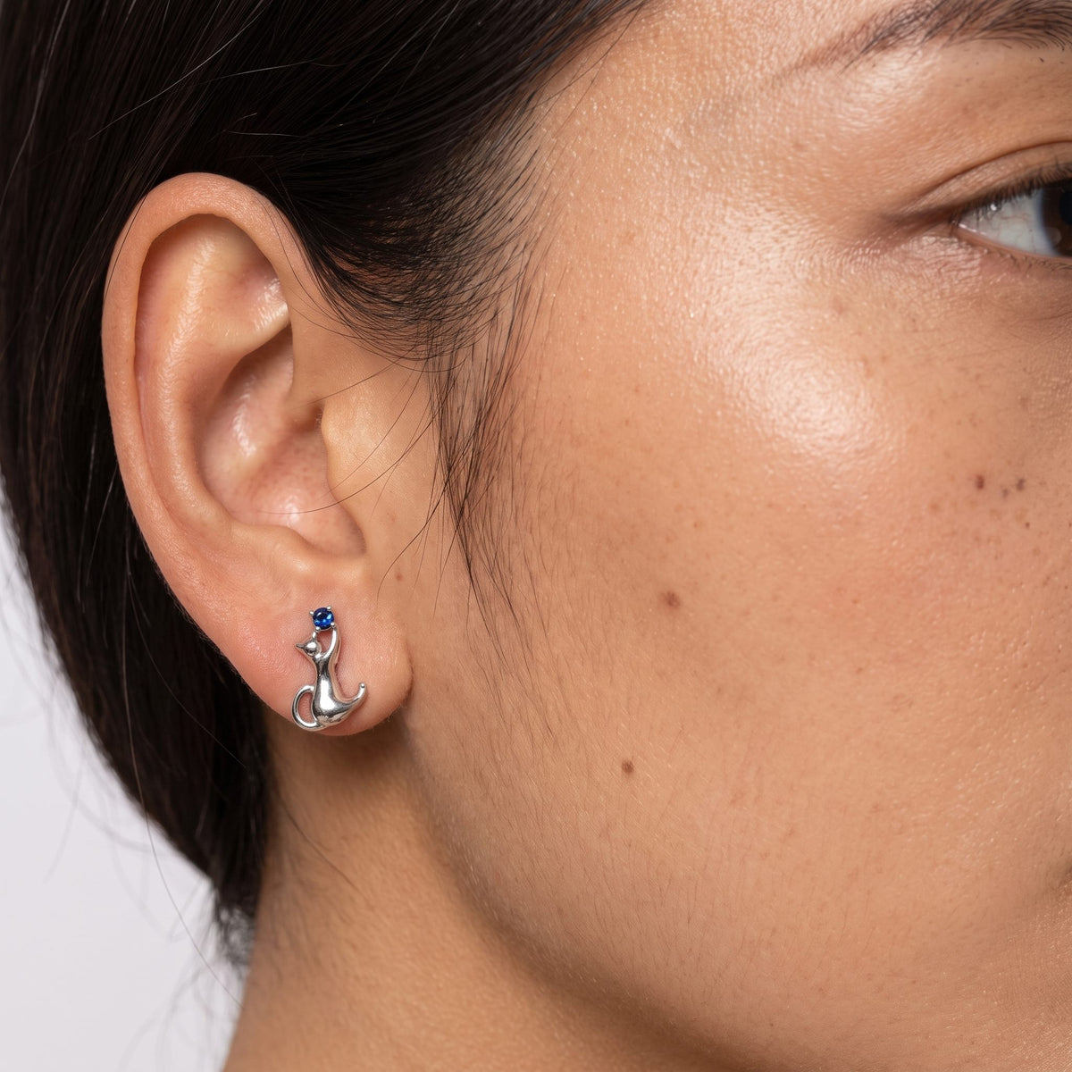 Woman wearing the Lilou Silver Kitten Earrings on her lobe, featuring a silver cat shape with a blue stone
