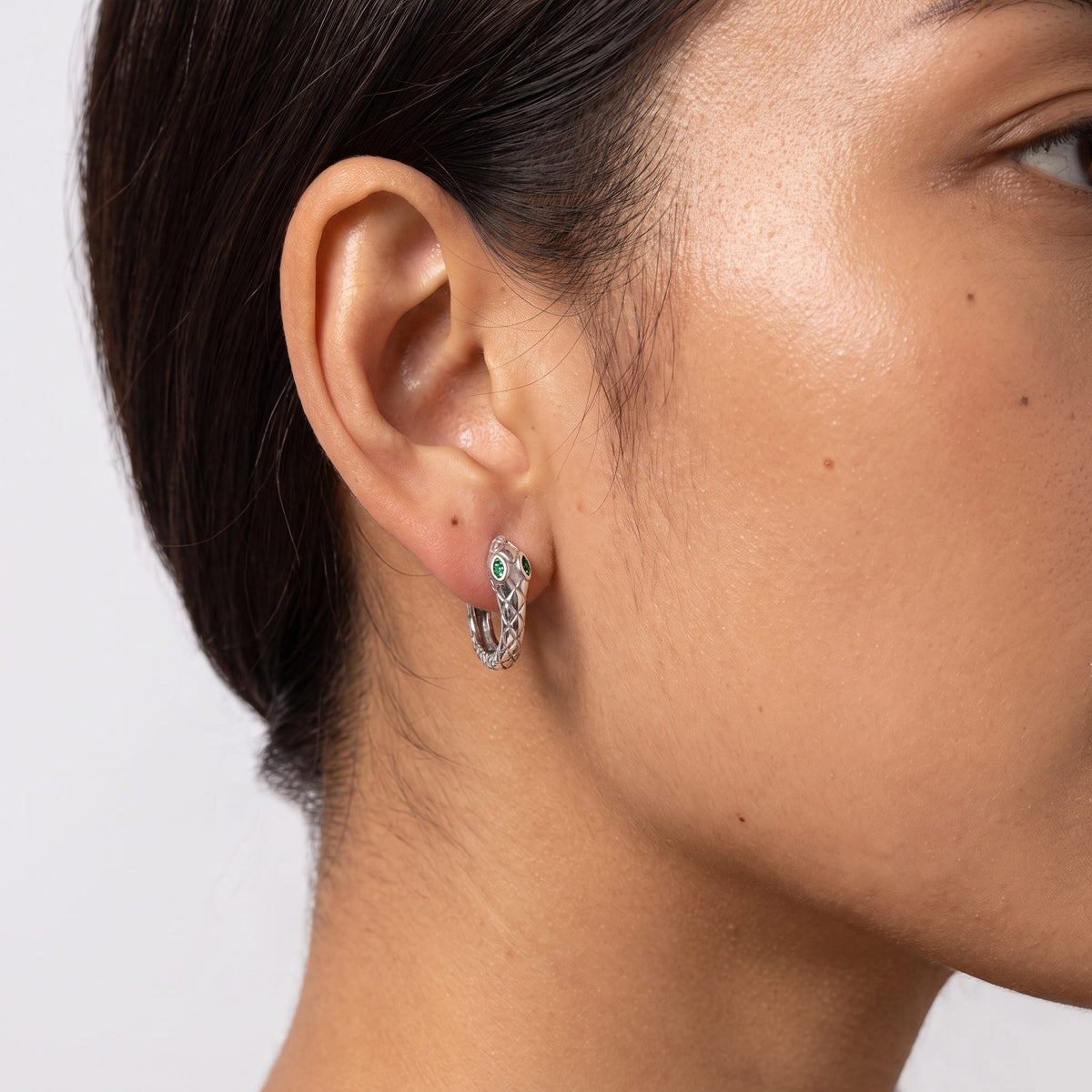 Close view of a woman wearing the Lilou Silver Snake Hoops through the lobe, featuring green stone eyes