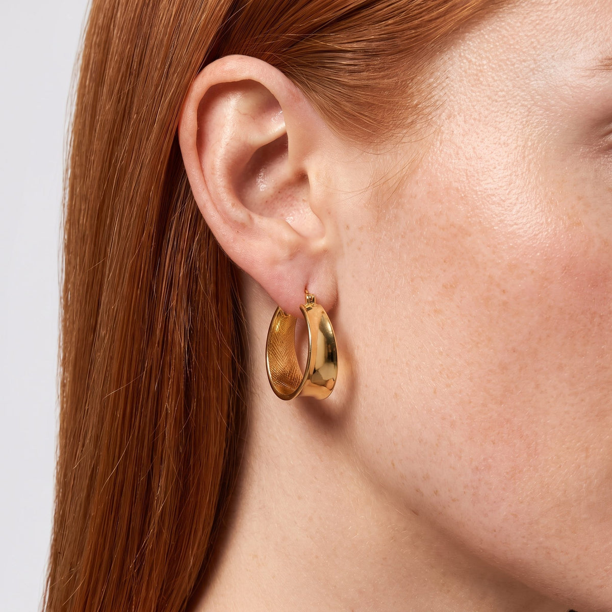 Woman wearing the Lyla Hoop Earrings through the lobe, showing their thick, shiny gold color band