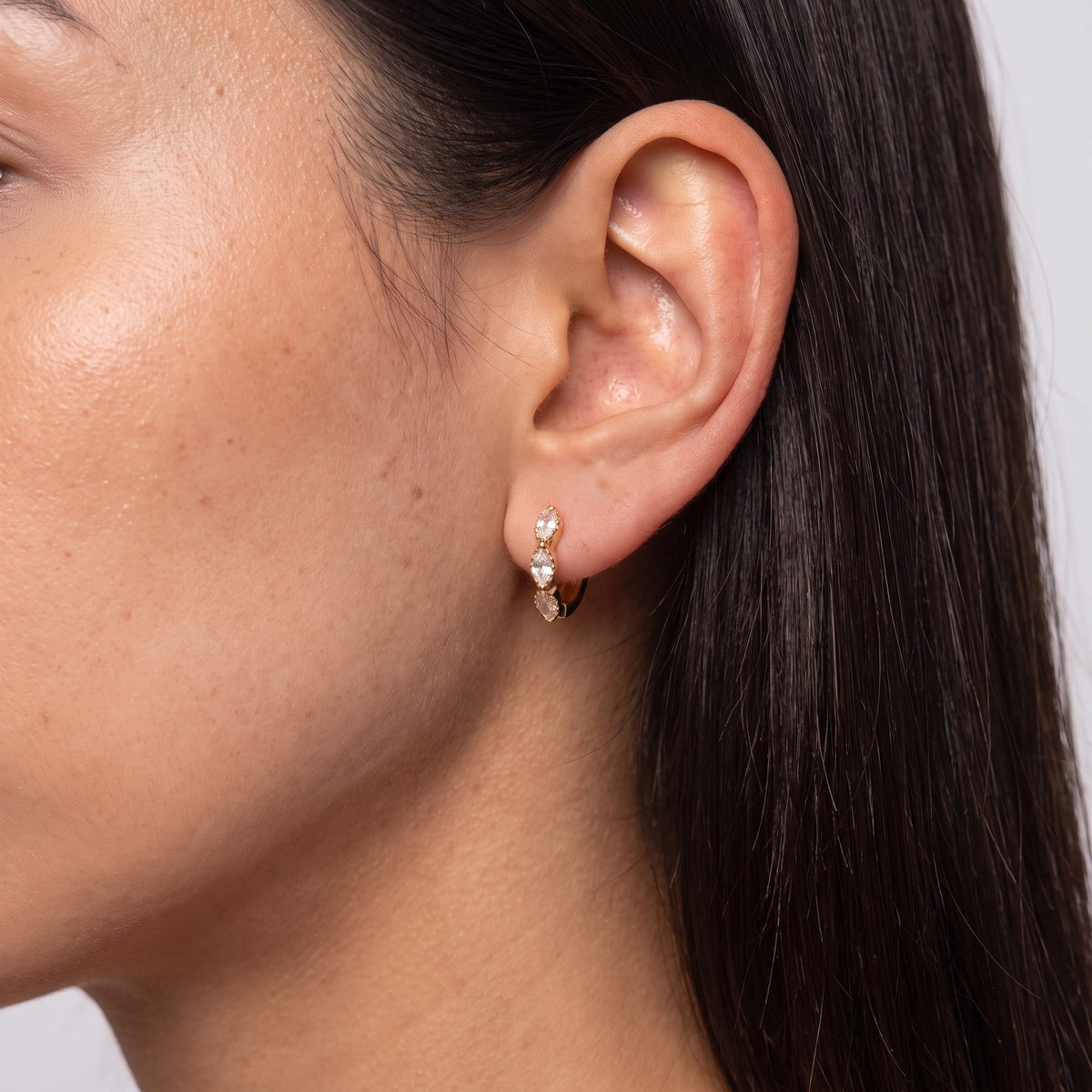 Woman wearing the Marquise Trio Huggies on the ear, her dark hair tucked behind it