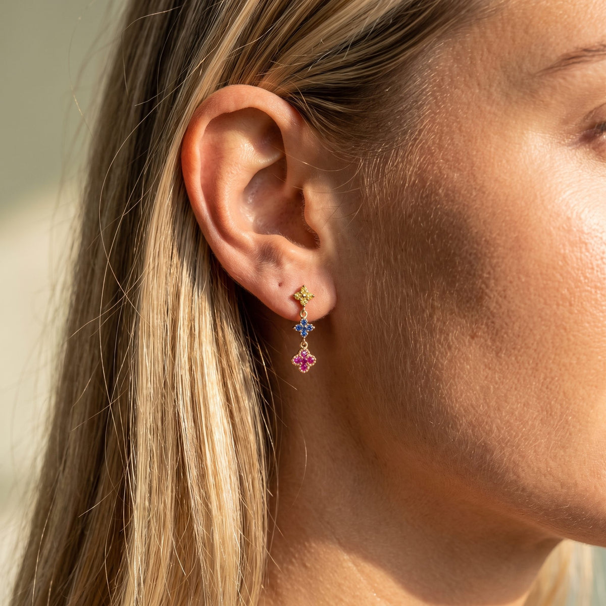 Woman wearing the Mia Glimmer Cluster Earrings hanging below the lobe with colorful flower-shaped charms