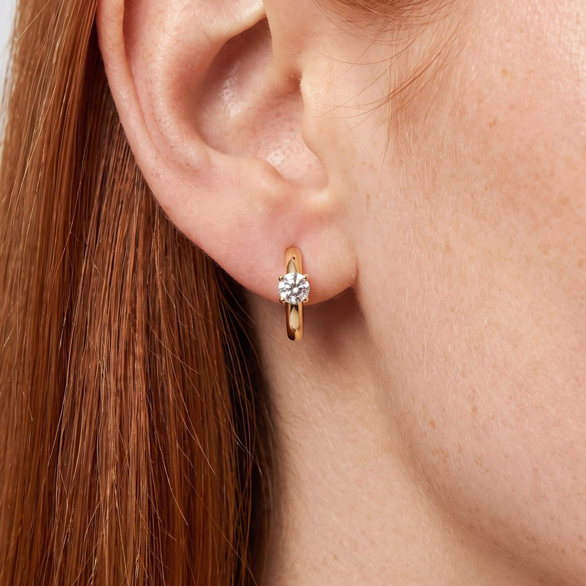 Woman wearing the Morgana Pixie Earrings through the lobe, featuring a gold-colored hoop with a single clear stone