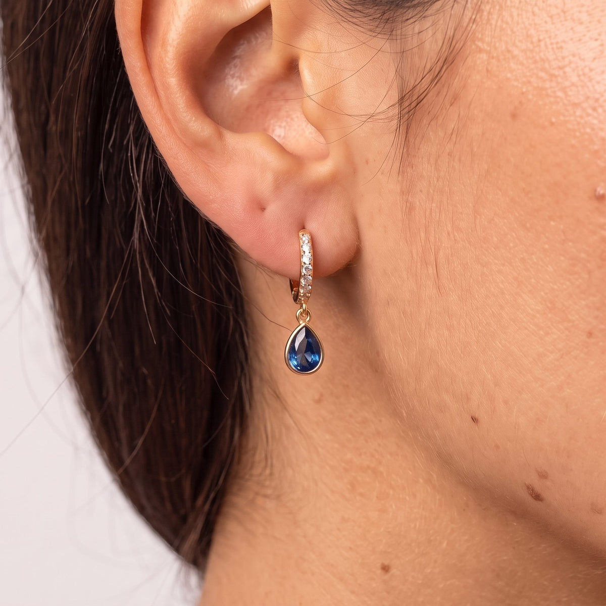 Close-up of the Navy Teardrop Huggies worn on the ear, showcasing the dangling blue crystal charm, in rose gold