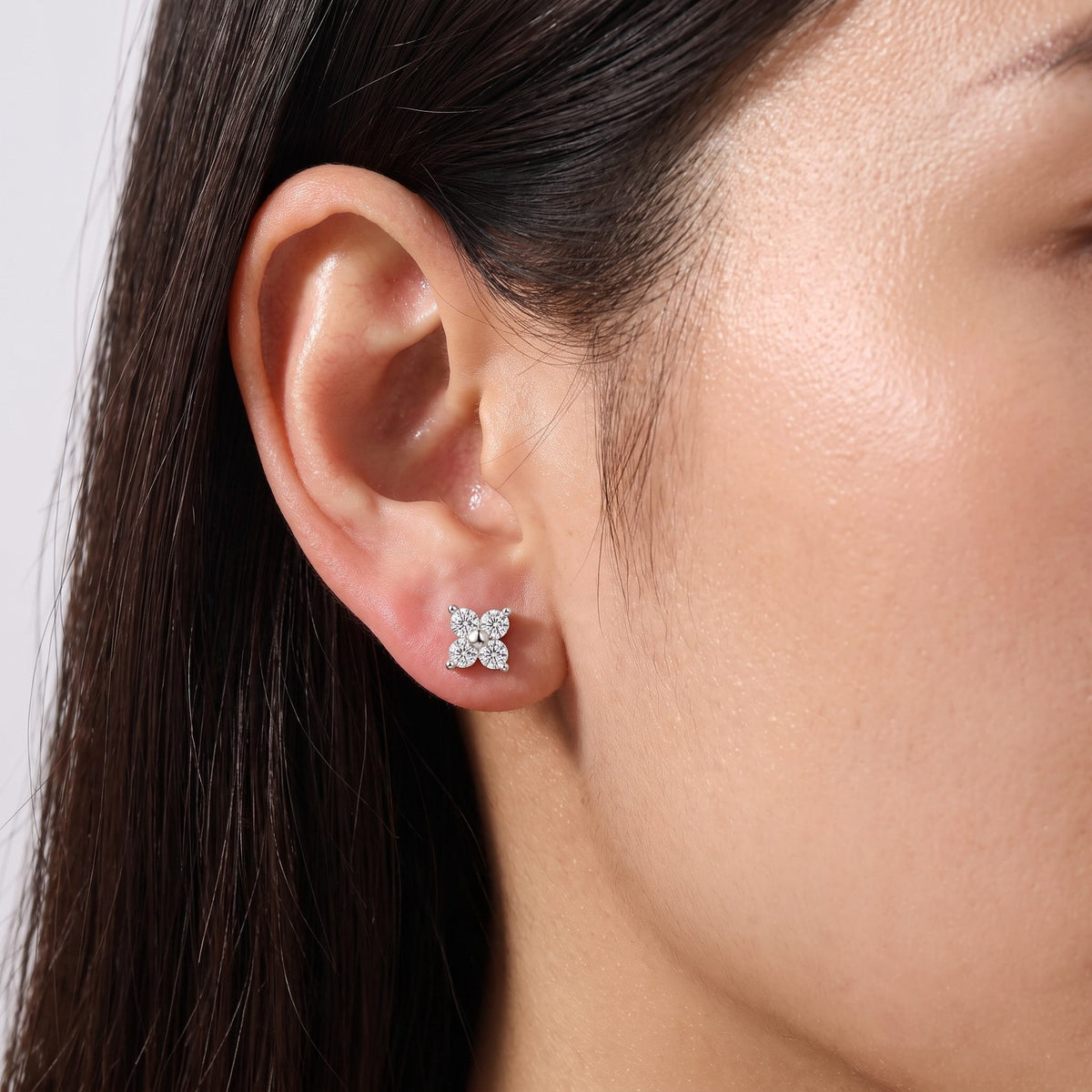 Close view of a woman wearing the Noemi crystal clover silver stud earrings on the ear