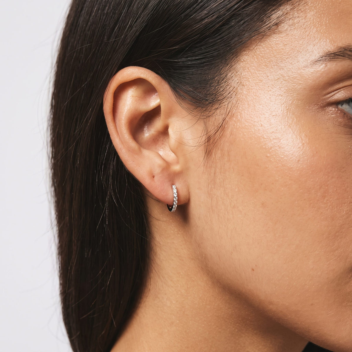 Woman wearing the Olivia Pavé Silver Hoops on her lobe, showcasing a row of tiny sparkling crystals