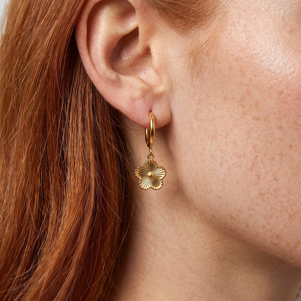 Woman wearing the Rowena Flower Hoop Earrings hanging below the lobe with a gold textured flower charm