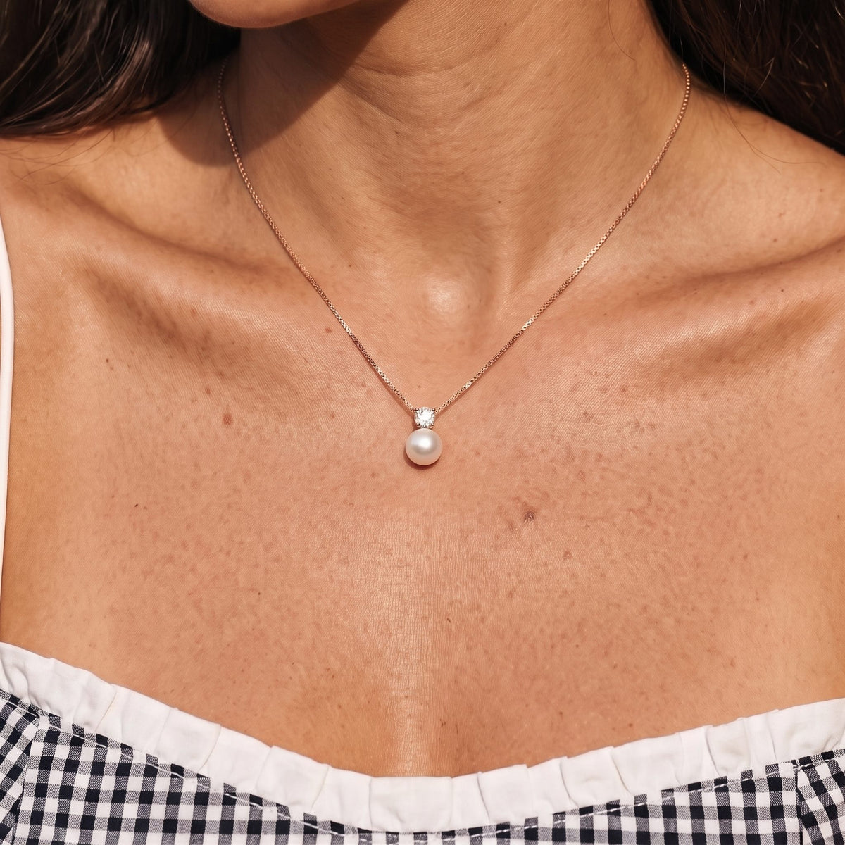 Close-up of the Pearl Pendant in rose gold at the collarbone, worn with a gingham top
