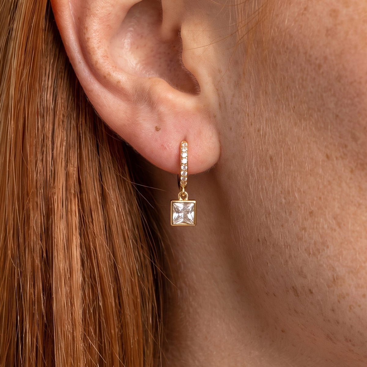 Close-up of the Square Crystal Huggies on the ear, featuring a dangling square crystal charm
