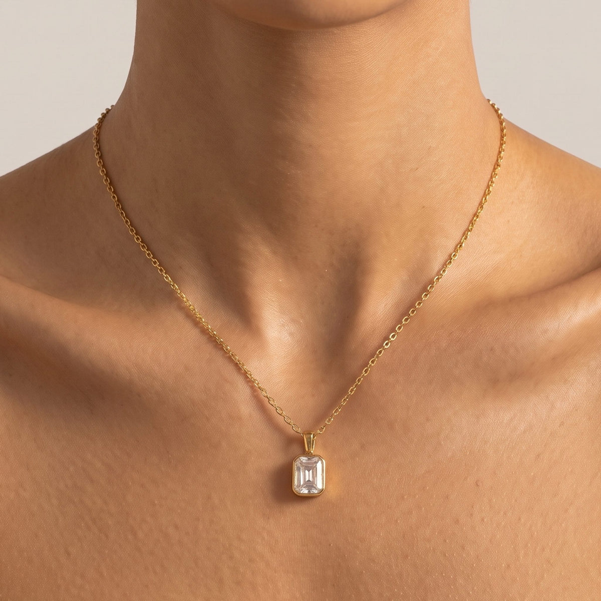 Close-up of the Step Cut Pendant at the collarbone featuring an emerald-cut crystal stone in a gold setting