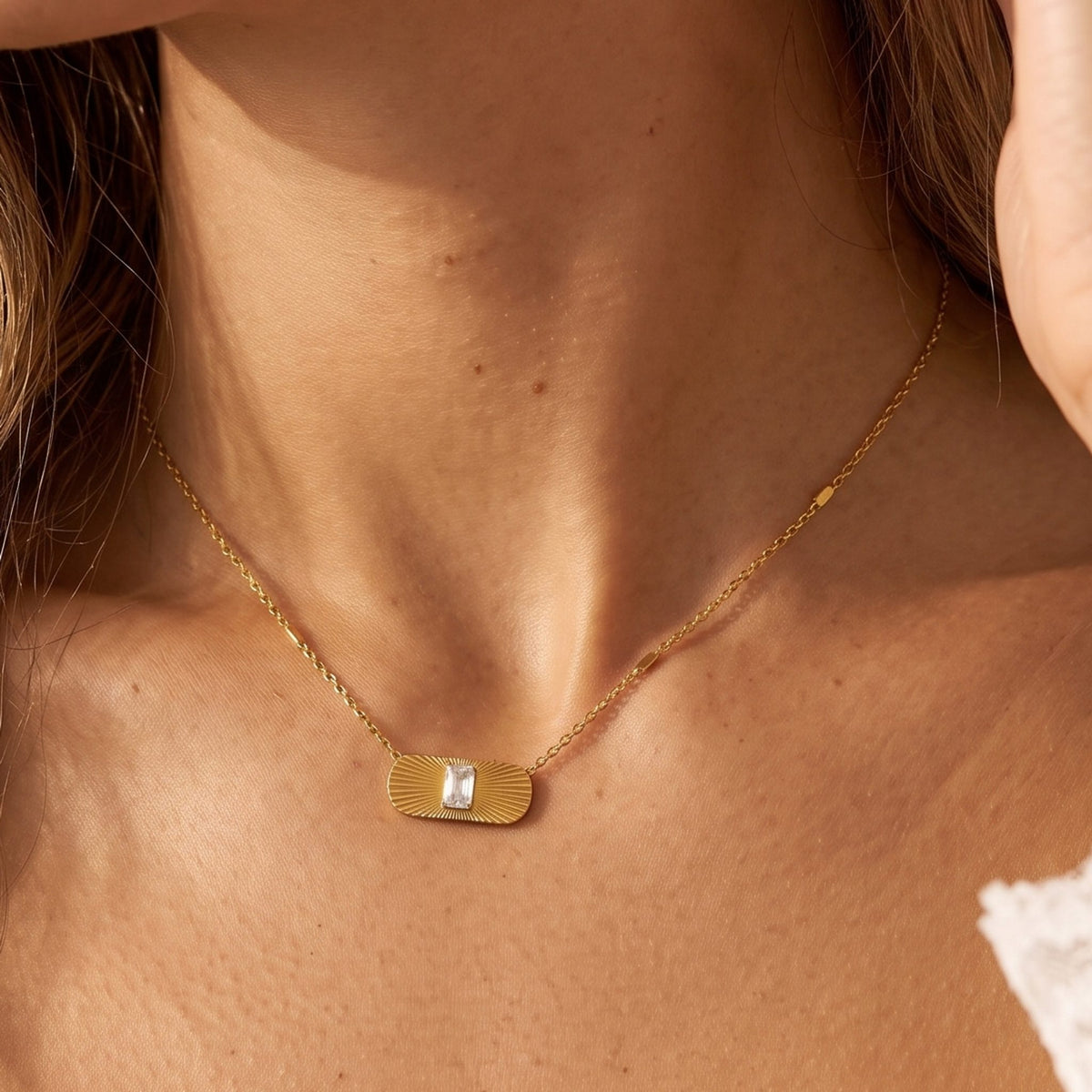 Close-up of the Sunburst Tag Necklace at the collarbone, highlighting its center crystal under warm light